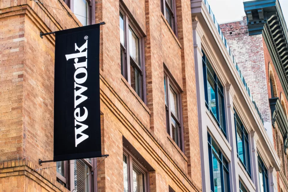 The sign for a WeWork office appears at the exterior of a brick high-rise in a dense downtown.